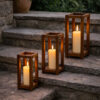 Trois lanternes en bois avec bougies allumées, disposées sur des marches en pierre dans un décor extérieur