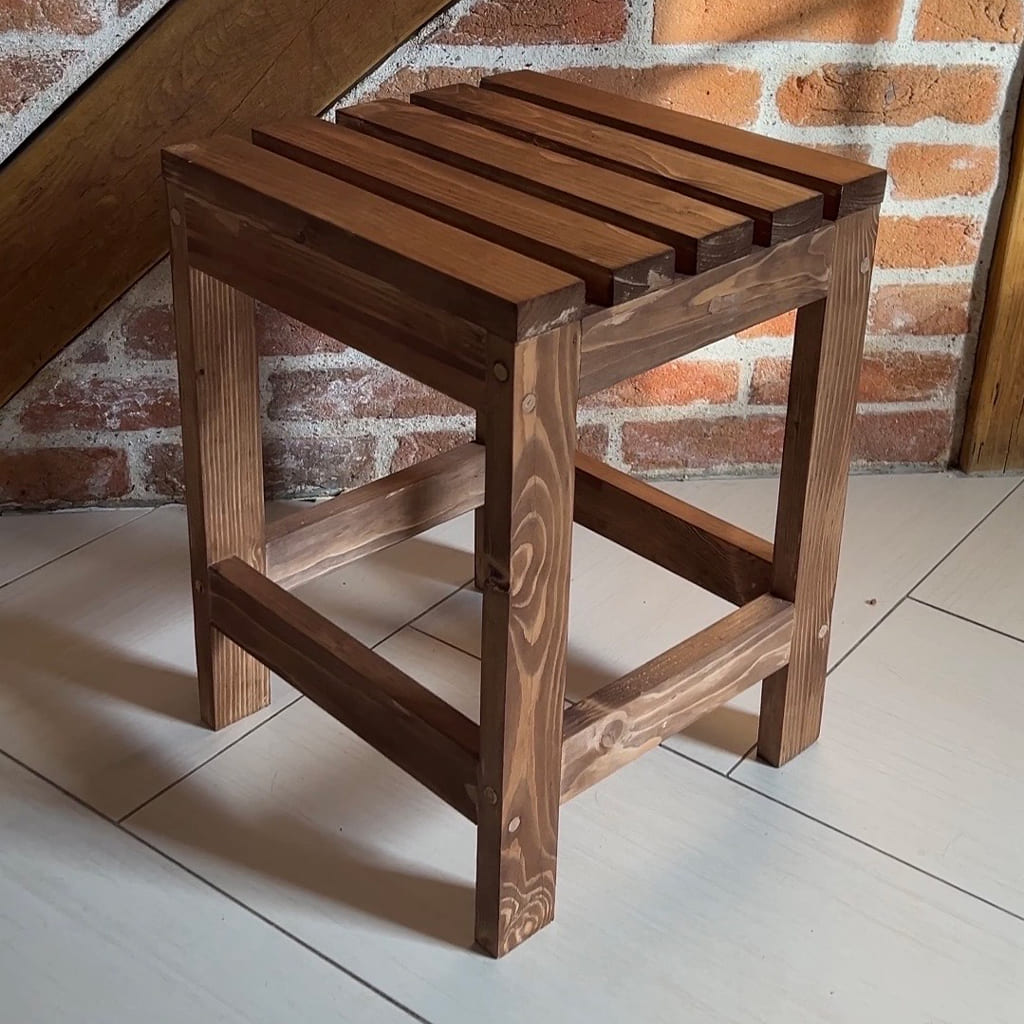 Tabouret en bois massif mis en scène dans un intérieur rustique, posé devant un mur en briques