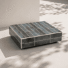 Bloc rectangulaire recouvert de carreaux verts foncés, posé sur une surface claire avec des ombres végétales projetées.