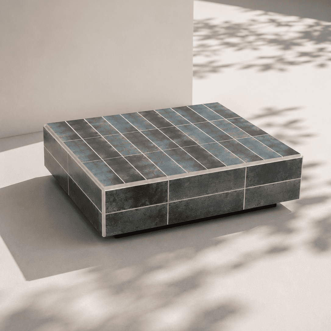 Bloc rectangulaire recouvert de carreaux verts foncés, posé sur une surface claire avec des ombres végétales projetées.